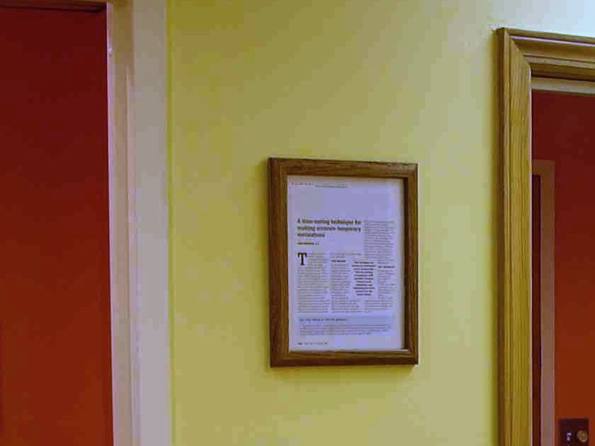 The yellow wall behind the front desk, with a framed journal article, between two orange rooms
