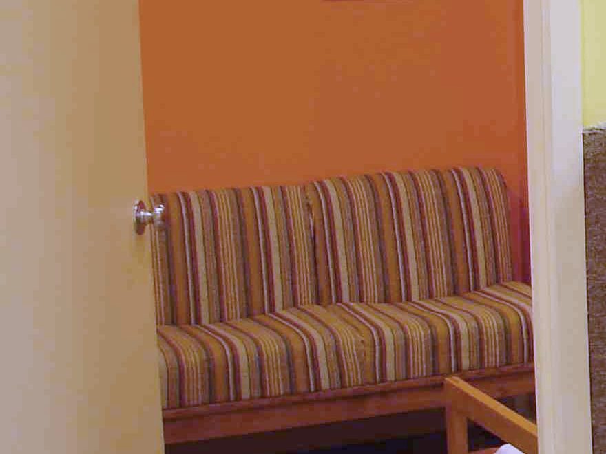 A seating area with a striped sofa against an orange wall, seen through the open doorway beside the front desk