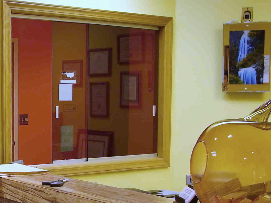 The front desk at Sunbeam Dental: a wood counter with an amber glass jar, the reception window and a framed waterfall picture on the yellow wall