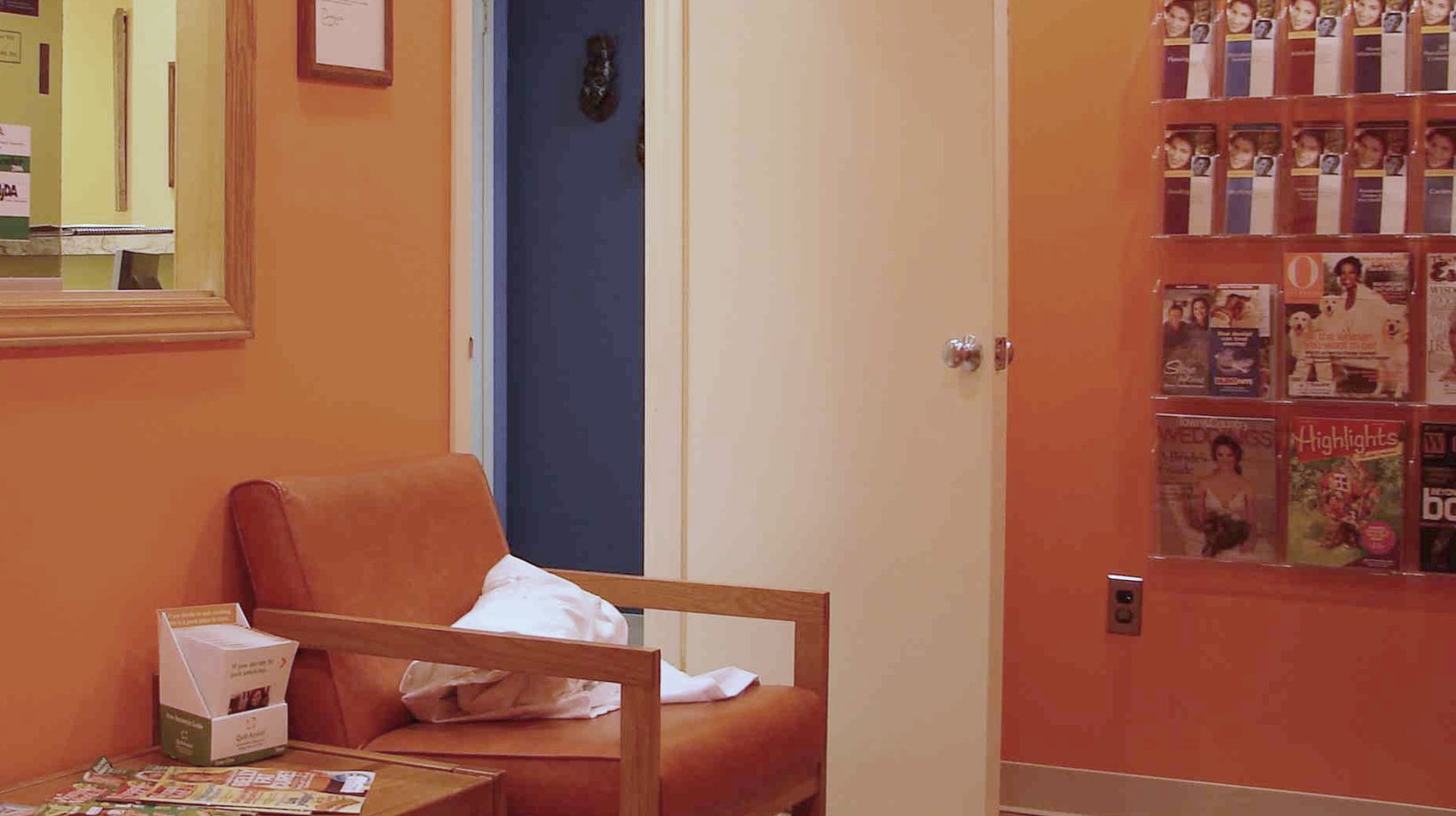 The orange waiting room at Sunbeam Dental, with an armchair and a rack of magazines